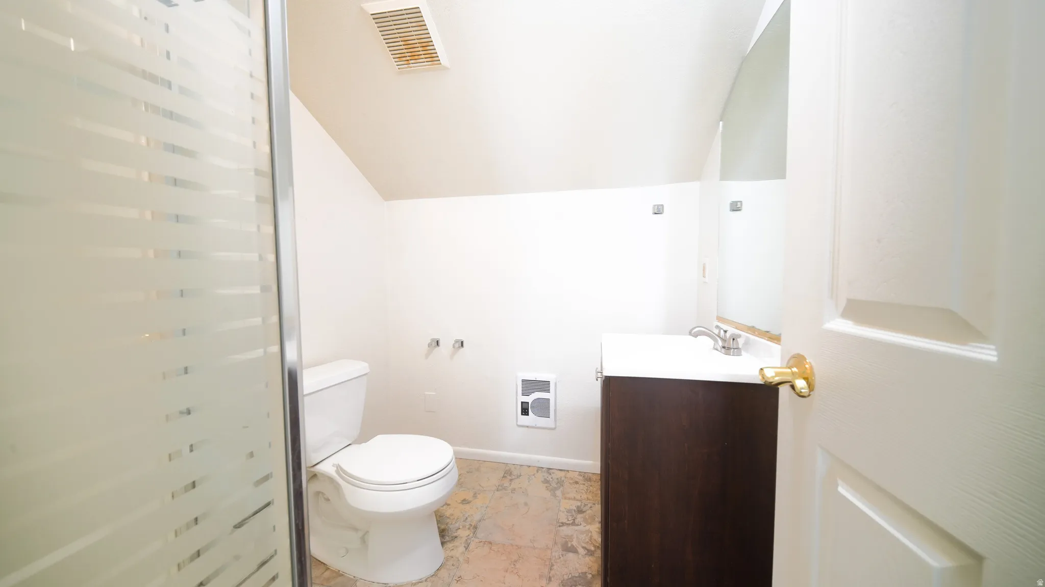 Enclosed shower with frosted glass, single vanity with integrated sink, toilet, wall-mounted mirror, and tile flooring