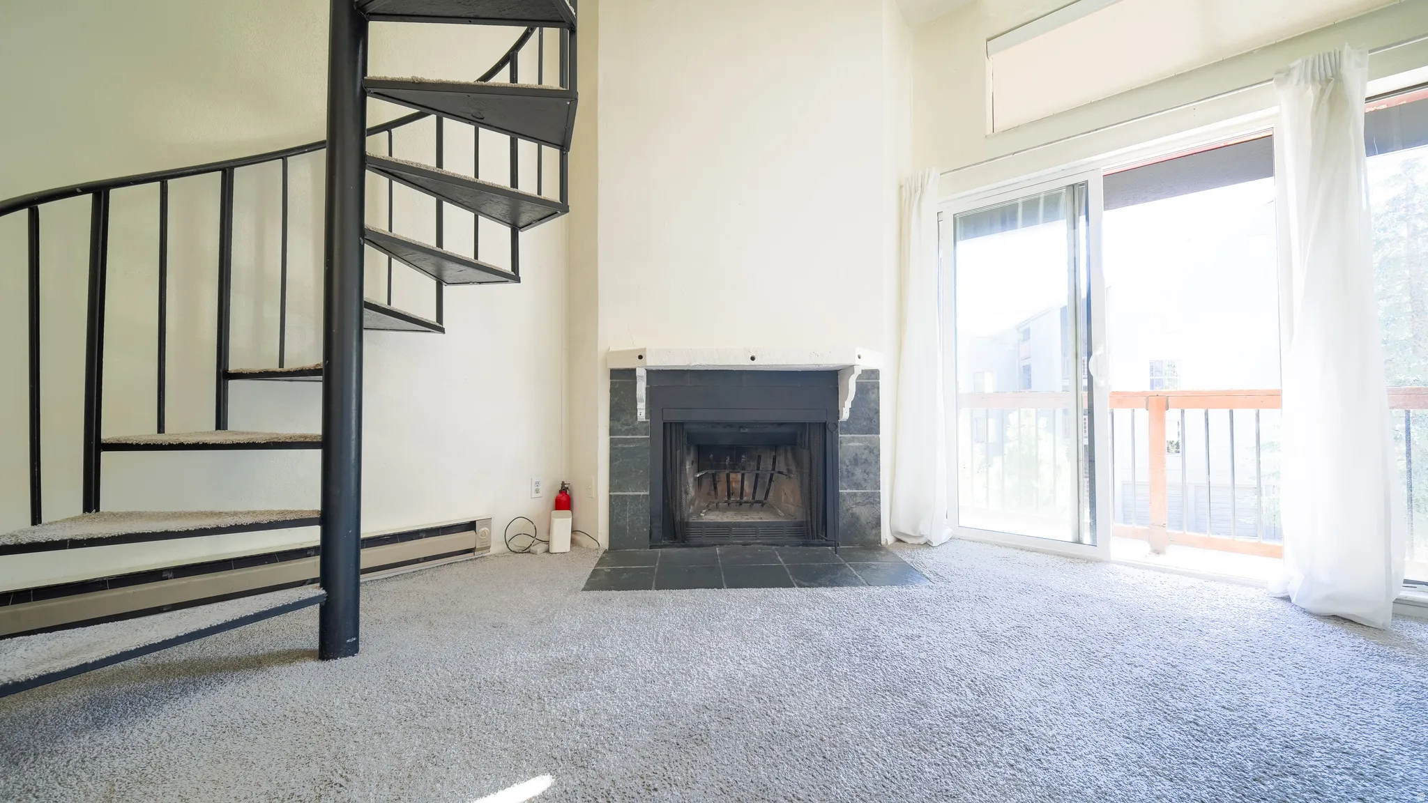 Spiral staircase with black metal railing, fireplace with stone surround, and sliding glass door