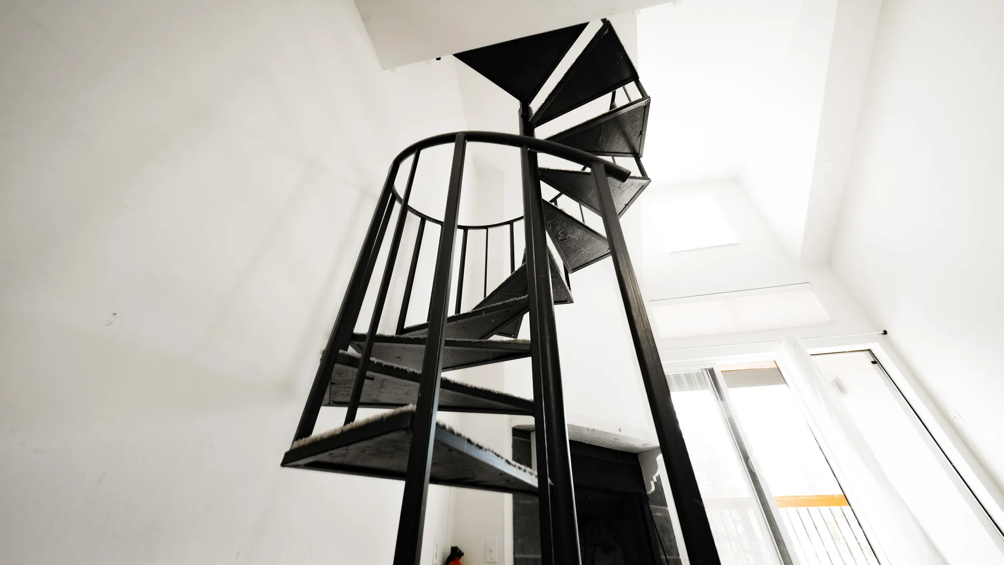 Black metal spiral staircase with open risers, a high ceiling, and a skylight