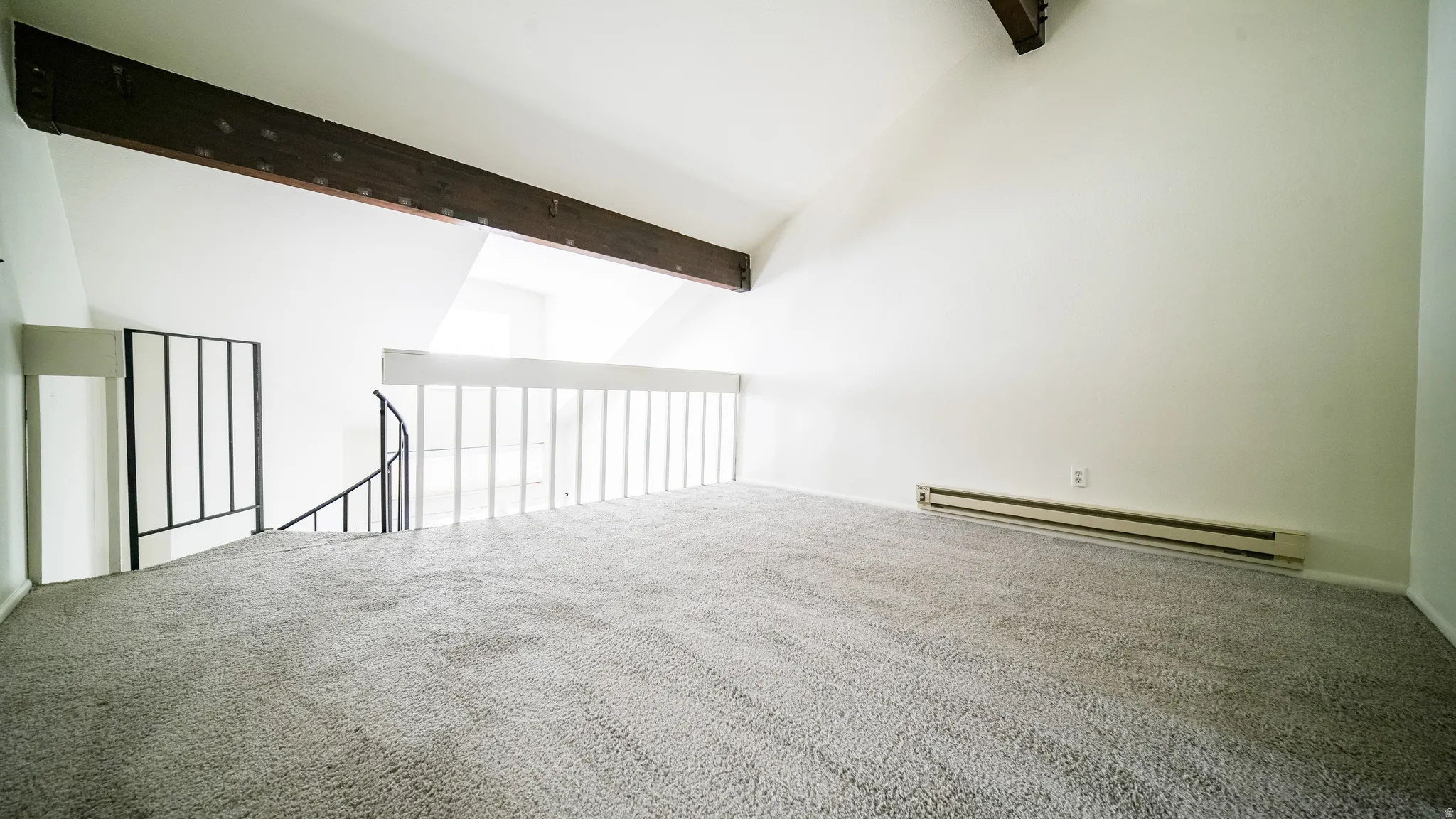 Vaulted ceiling with exposed wood beam, spiral staircase with metal railing, white wall paneling, and neutral carpeting
