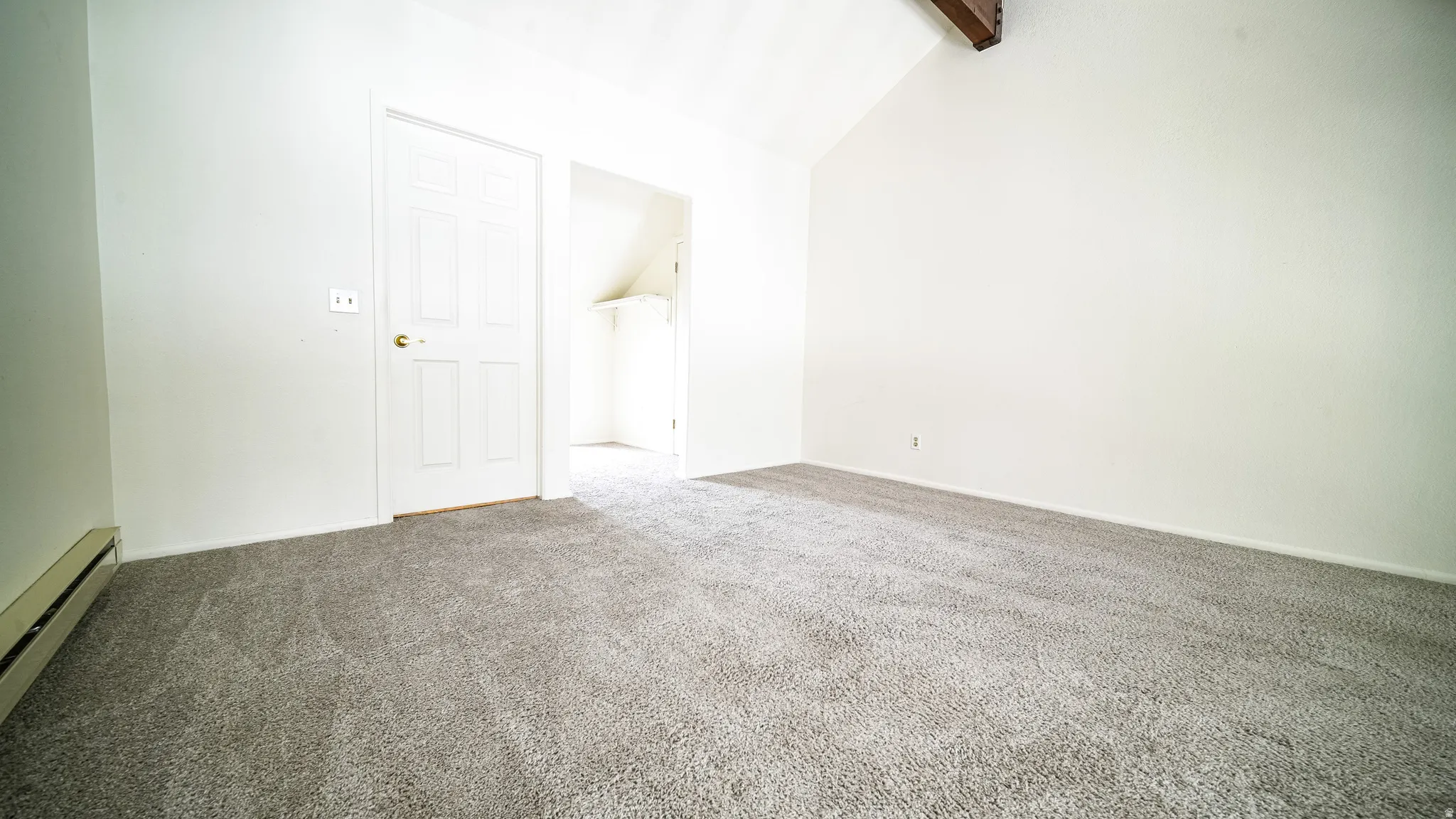 Vaulted ceiling with exposed wood beam, wall-to-wall carpeting, and white painted walls