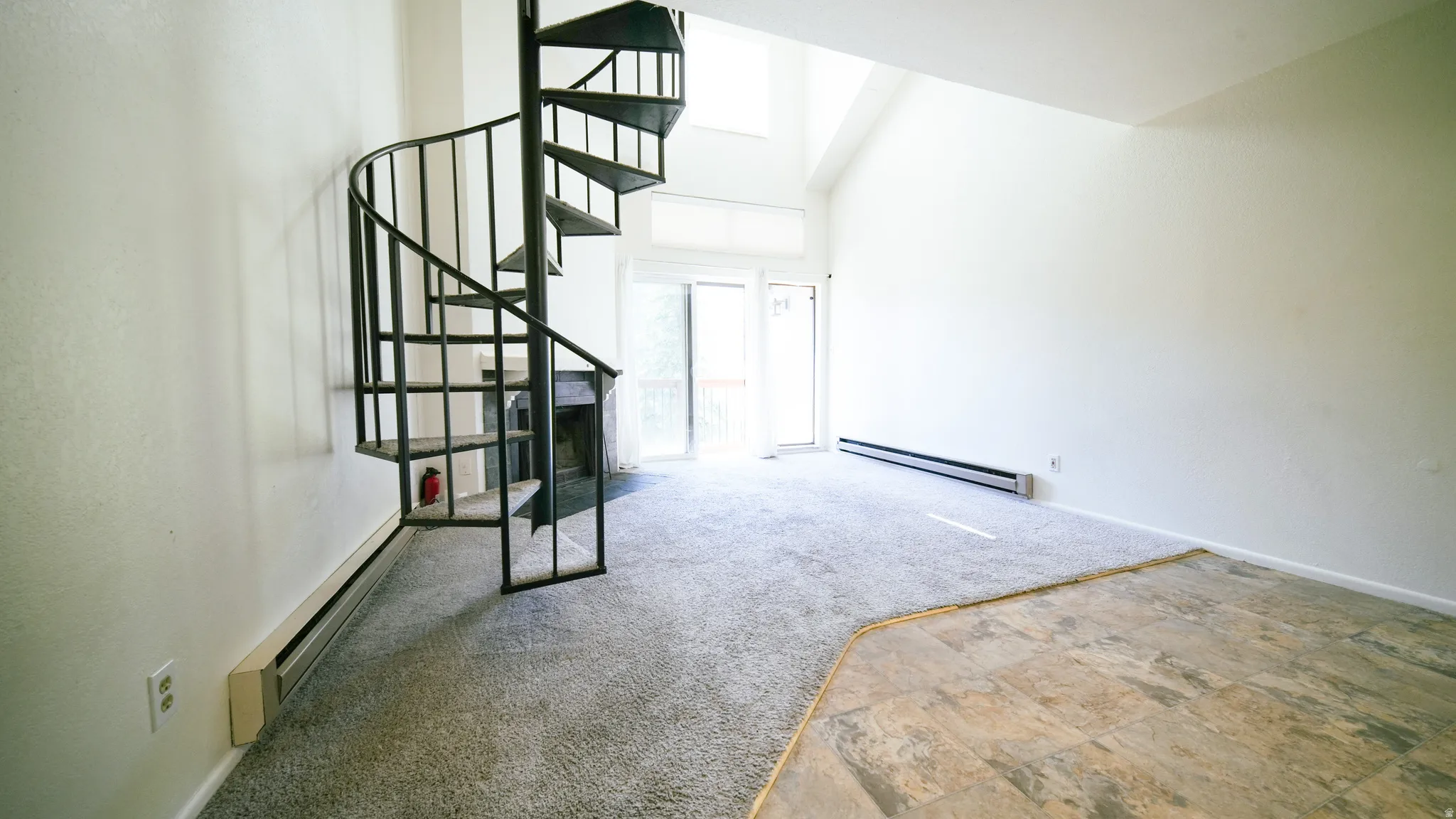 Spiral staircase with metal railing, vaulted ceiling, sliding glass door, fireplace, and mixed flooring