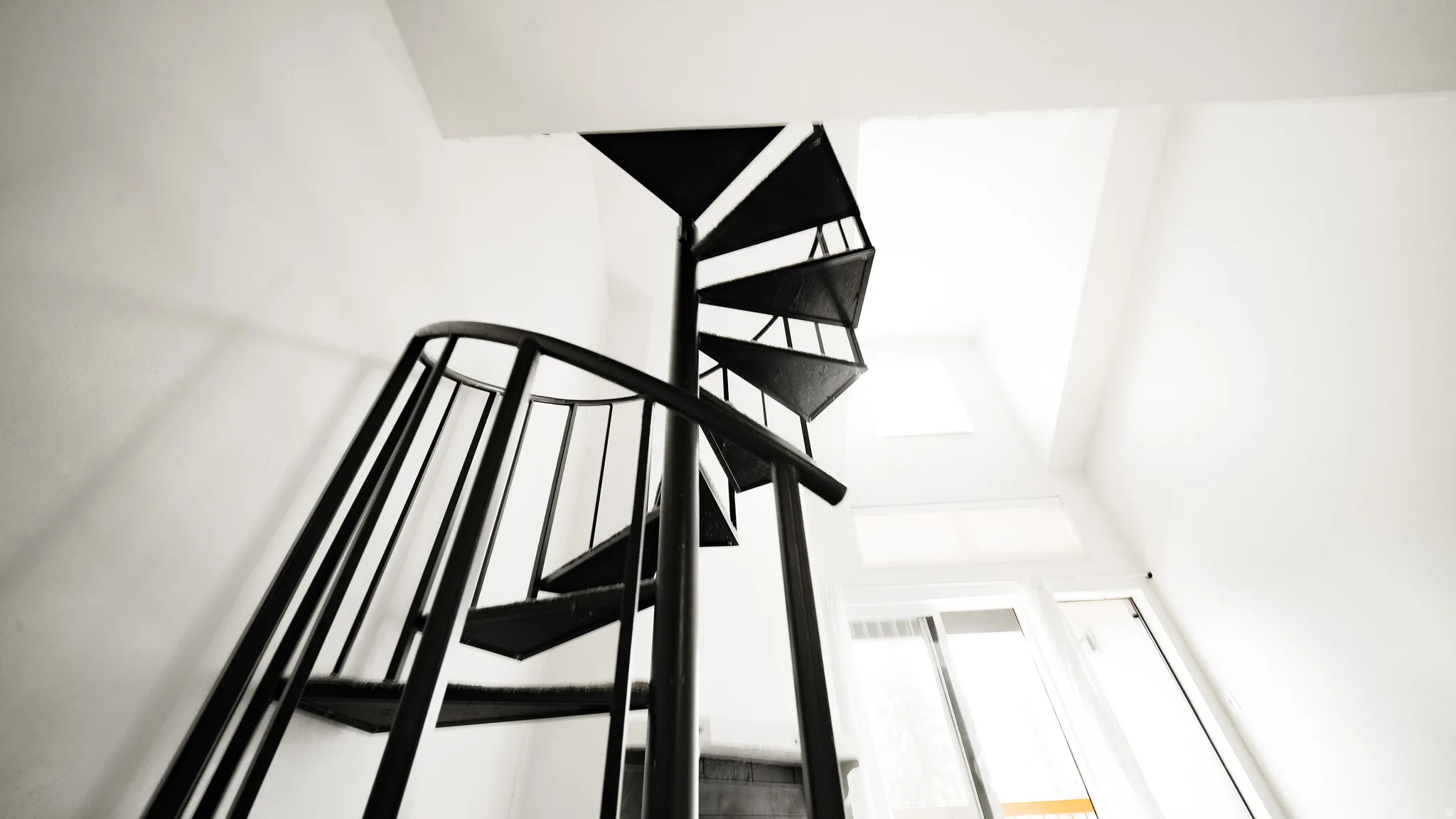 Black spiral staircase with open risers and railing, complemented by a skylight and a white window frame