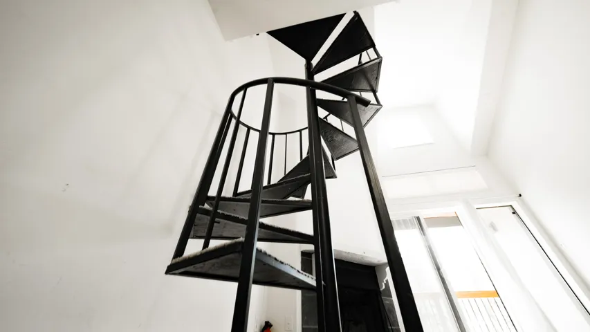 Black metal spiral staircase with open risers, a high ceiling, and a skylight