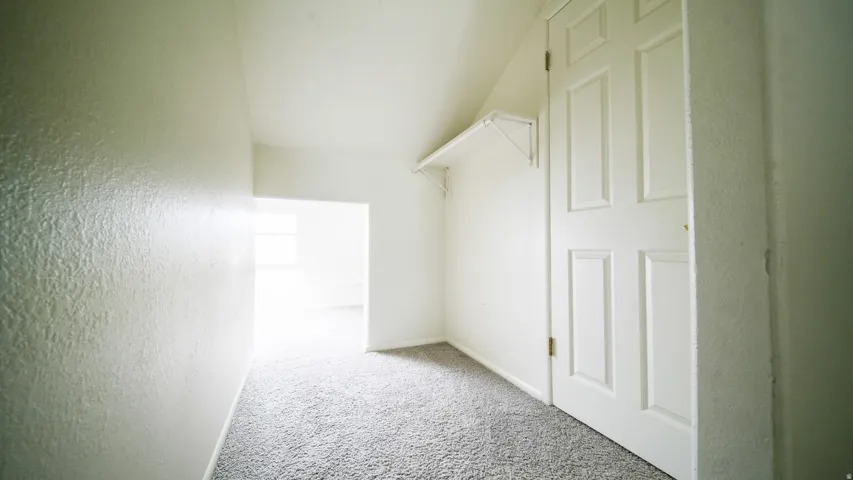 Light grey carpeting, textured white walls, white paneled door, and built-in white shelving