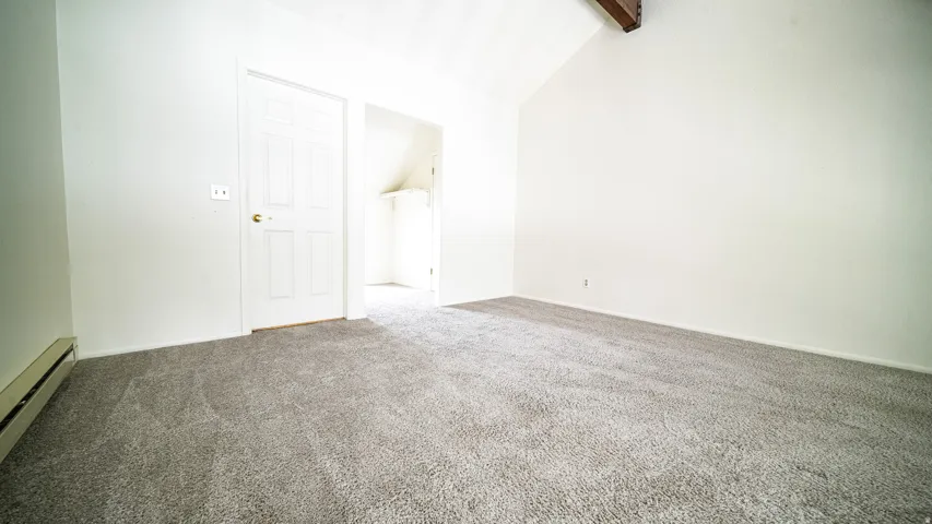 Vaulted ceiling with exposed wood beam, wall-to-wall carpeting, and white painted walls