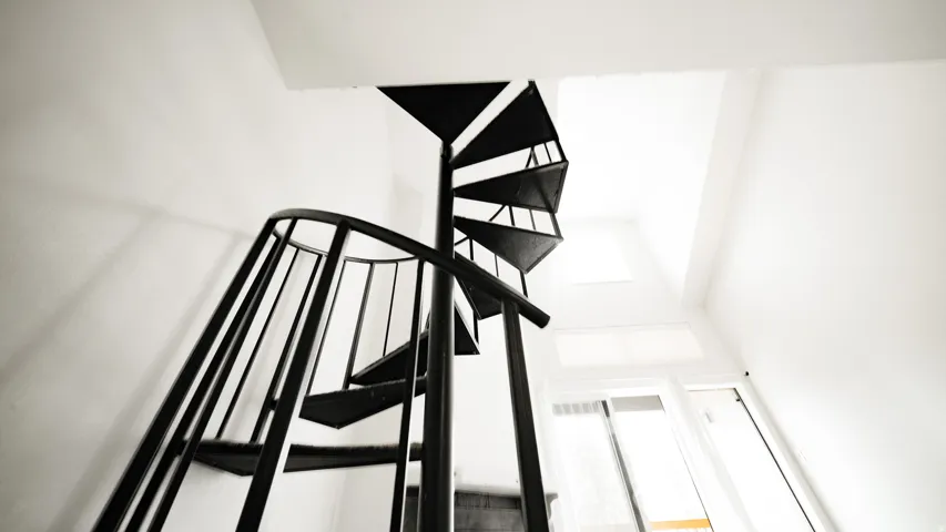Black spiral staircase with open risers and railing, complemented by a skylight and a white window frame