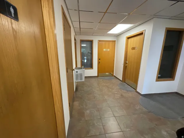 Hallway featuring tile flooring, multiple wood doors, a built-in water cooler, and recessed lighting