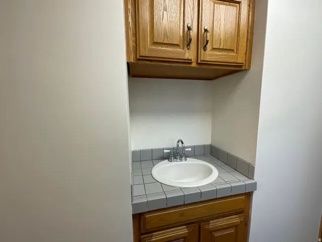Built-in vanity with wood-finish cabinetry, a drop-in sink, and a tile countertop