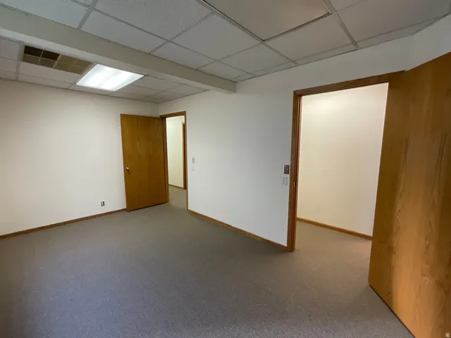 Carpeted flooring, white walls, wood trim, and drop ceiling with integrated lighting