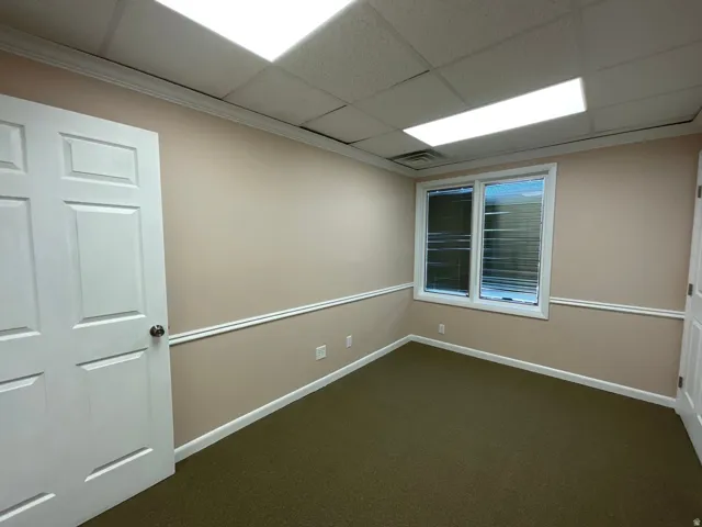 Recessed lighting, drop ceiling, window with horizontal blinds, wall-mounted electrical outlets, and neutral tone walls