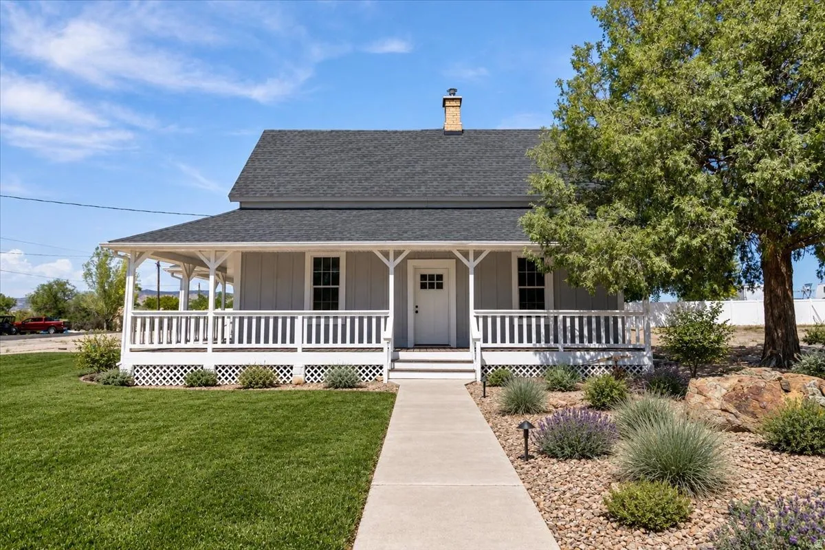 Gabled roofline with a chimney, a covered porch with white railings, and a concrete walkway