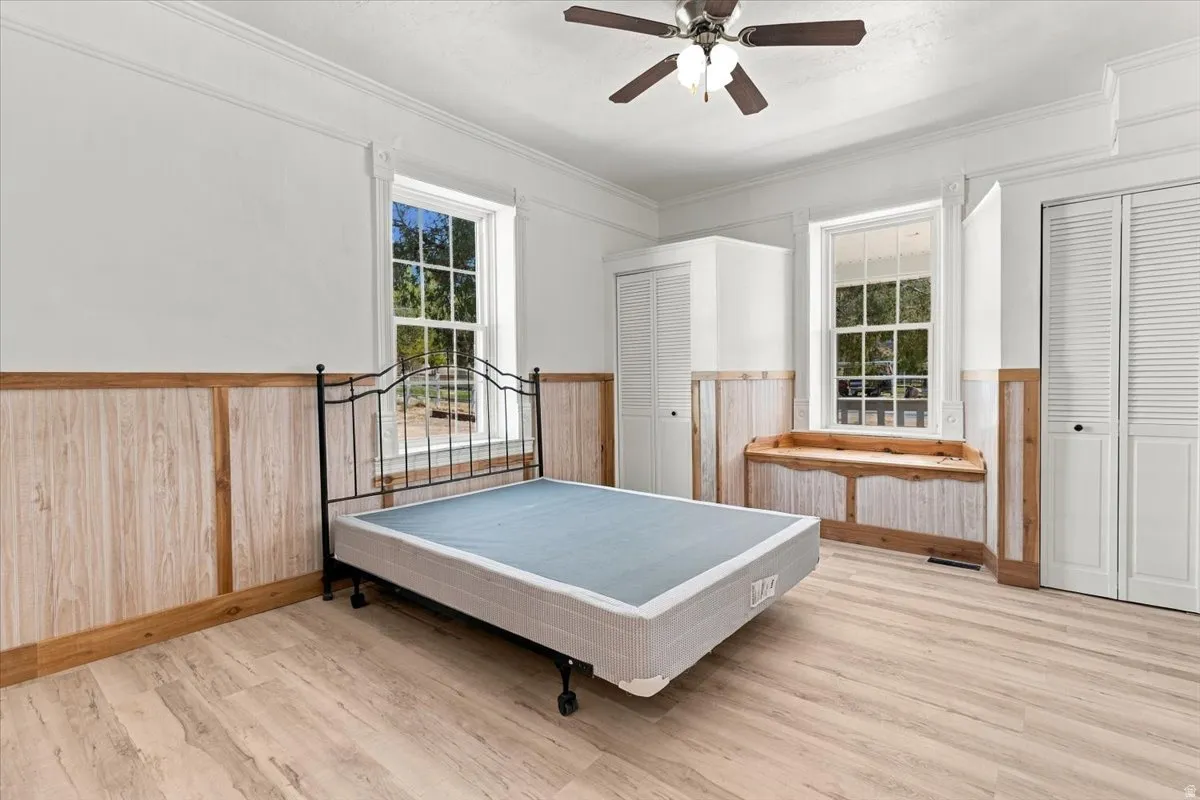 Wood-finish flooring, paneled wainscoting, and a ceiling fan with integrated lighting