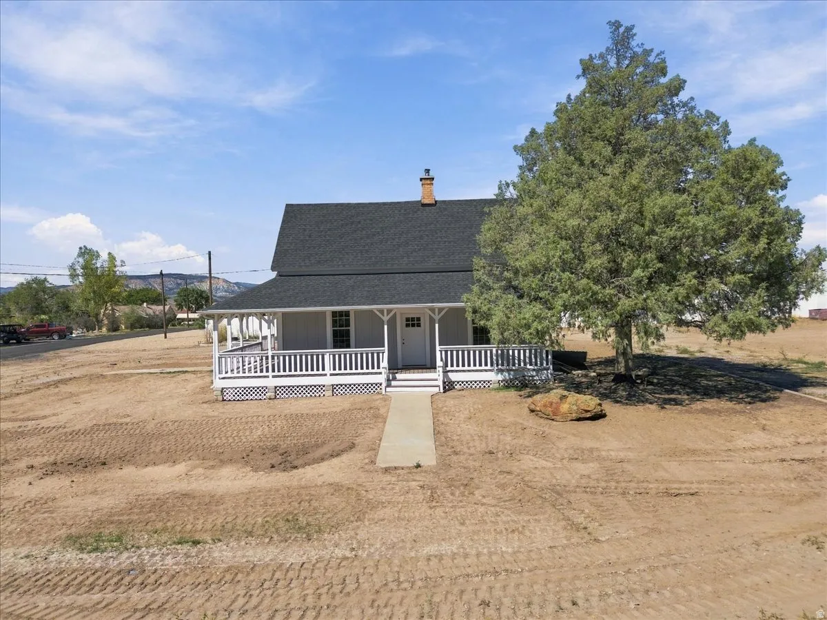 Traditional-style home featuring a covered front porch with white railings, a dark shingle roof, and a prominent front-facing chimney