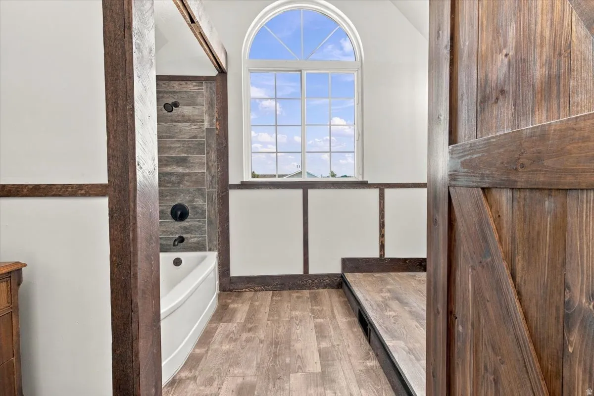 Arched window, wood-finish flooring, wood structural beams, ceramic tile shower surround, and a white soaking tub