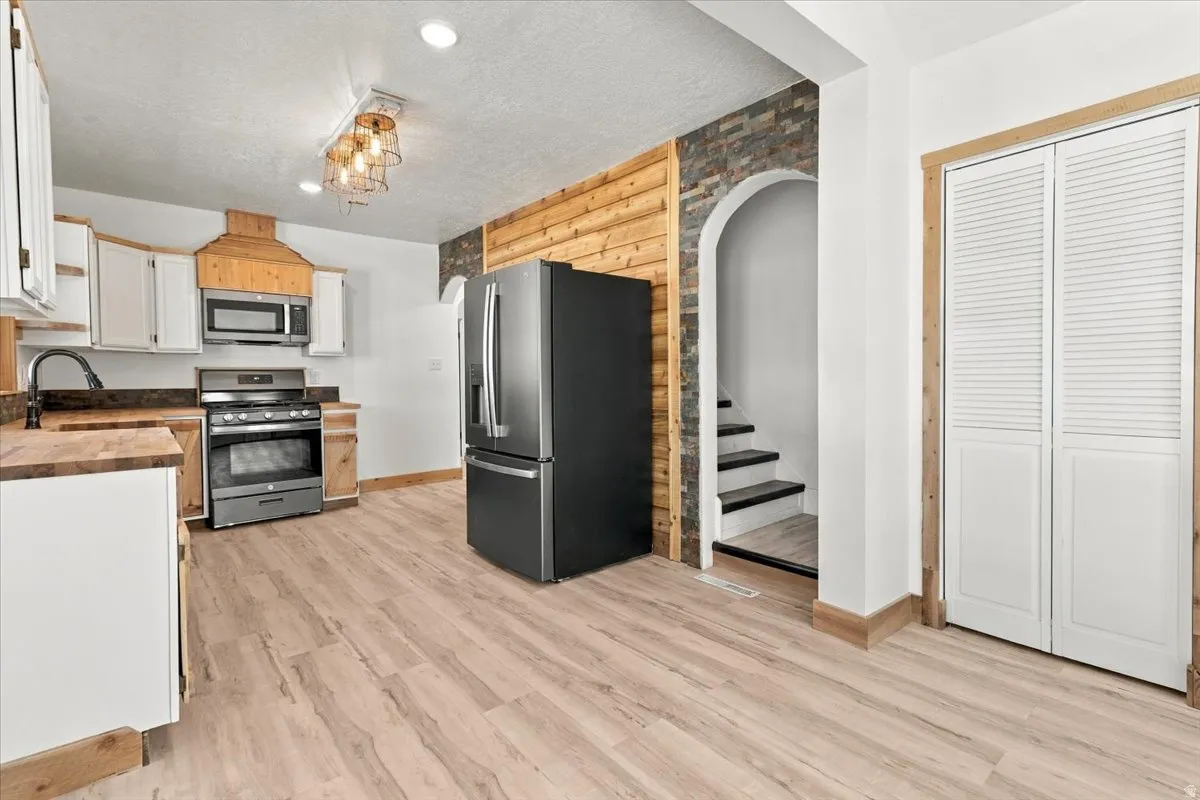 Contemporary kitchen featuring wood-finish flooring, white cabinetry, stainless steel appliances, and wood-toned countertops