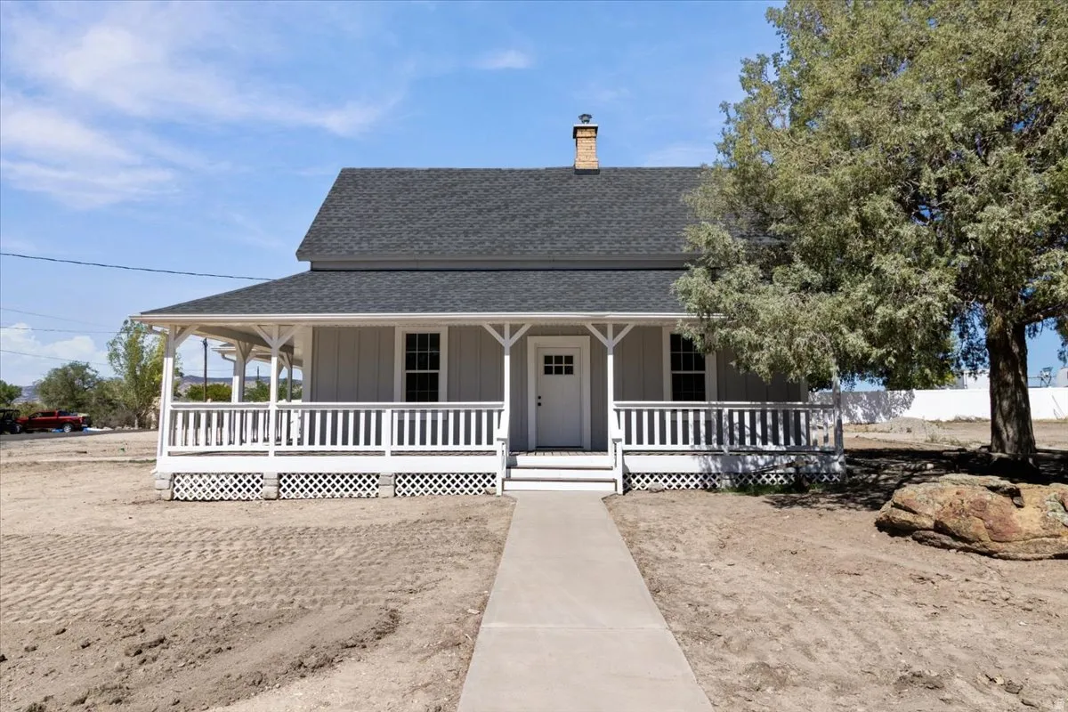 Front exterior featuring a covered porch with white railings, a gray siding facade, and a dark shingle roof
