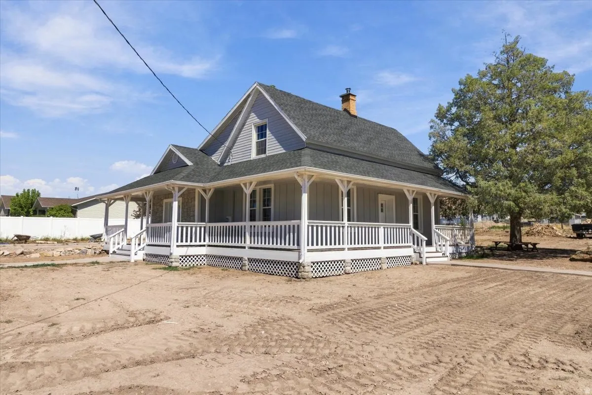 Expansive wrap-around porch with white railings, dormer window, and shingle siding