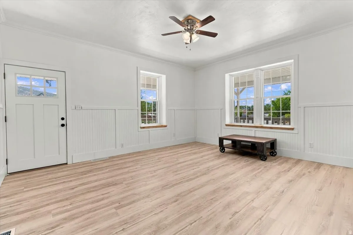 Light wood-finish flooring, white beadboard wainscoting, and a ceiling fan with light fixture