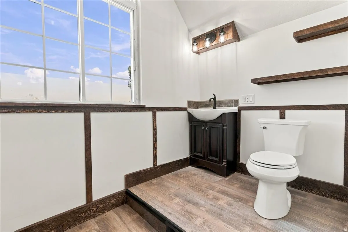 Wainscoting with dark wood trim, wood-finish flooring, a dark wood vanity with a basin sink, and a multi-pane window
