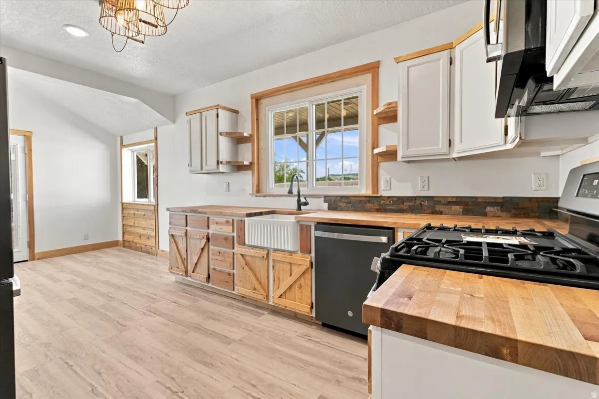 Kitchen featuring wood-finish flooring, natural wood countertops, white upper cabinetry, wood-paneled lower cabinetry, and a farmhouse sink