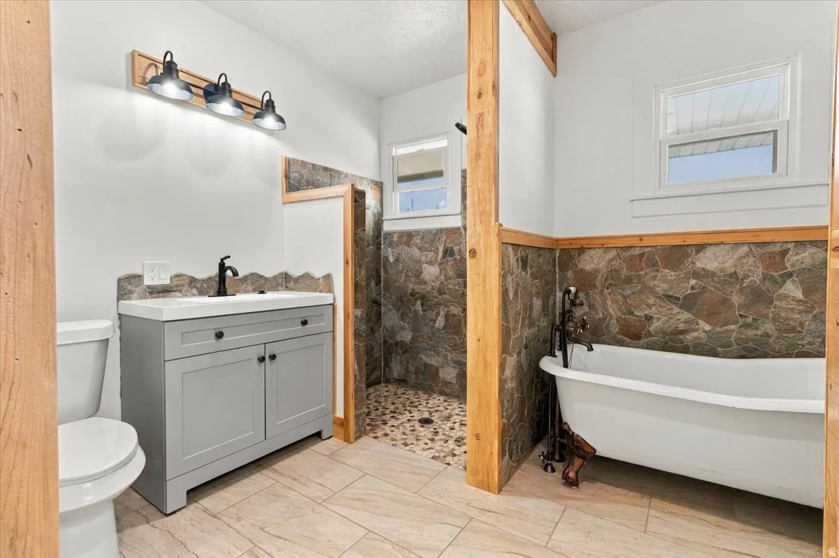 Stone accent walls, freestanding soaking tub, wood-finish flooring, custom wood trim, and a modern vanity