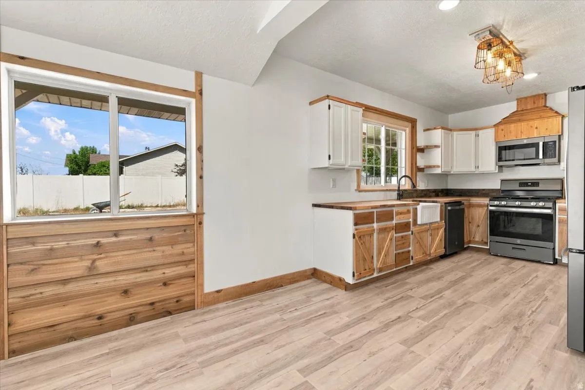 Kitchen featuring stainless steel appliances, a farmhouse sink, wood-finish flooring, white upper cabinetry, and wood-paneled lower cabinetry