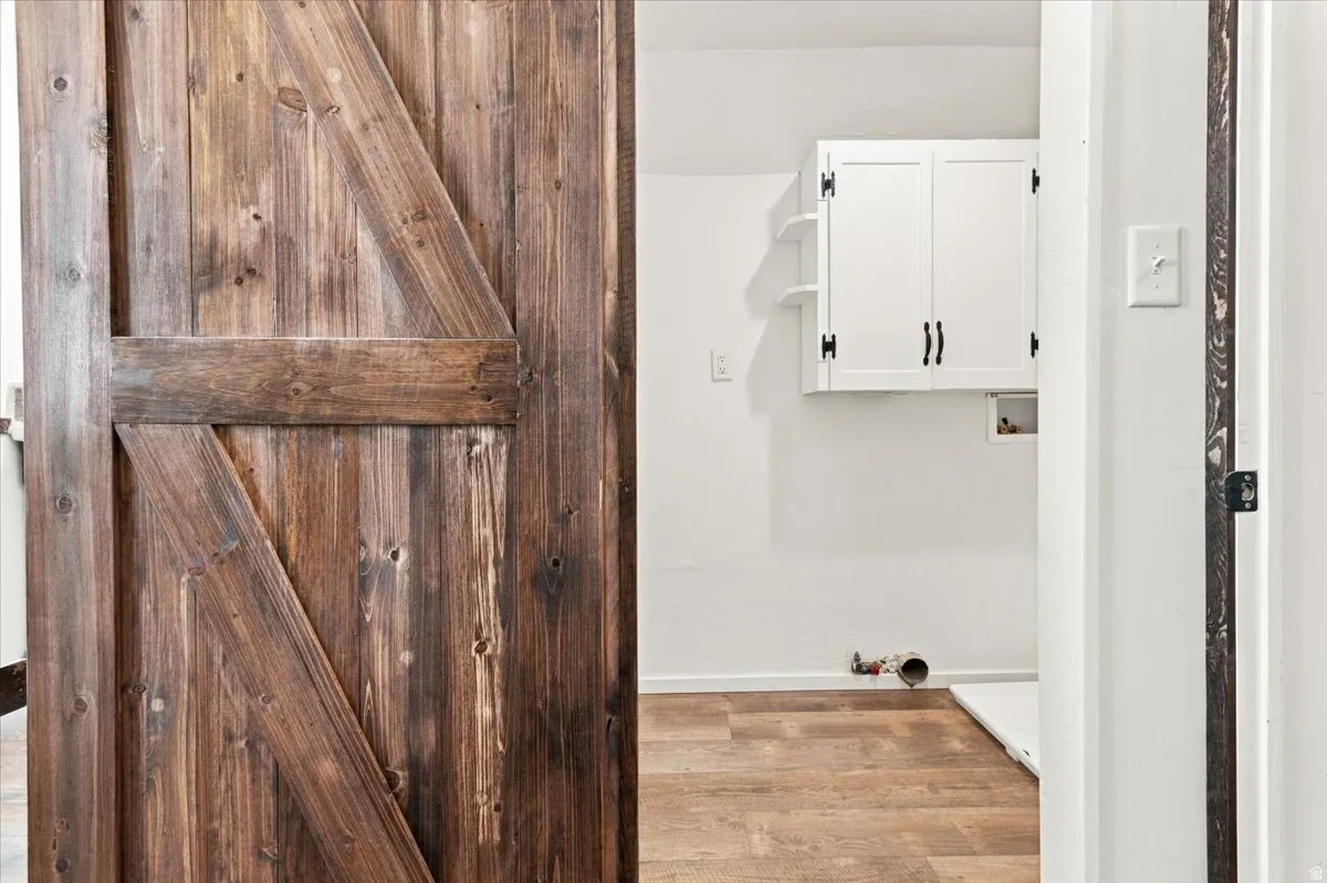 Rustic wood barn door with dark hardware, wood-finish flooring, white wall cabinetry, and open shelving