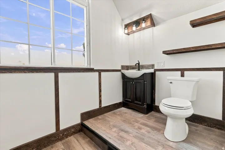 Wainscoting with dark wood trim, wood-finish flooring, a dark wood vanity with a basin sink, and a multi-pane window