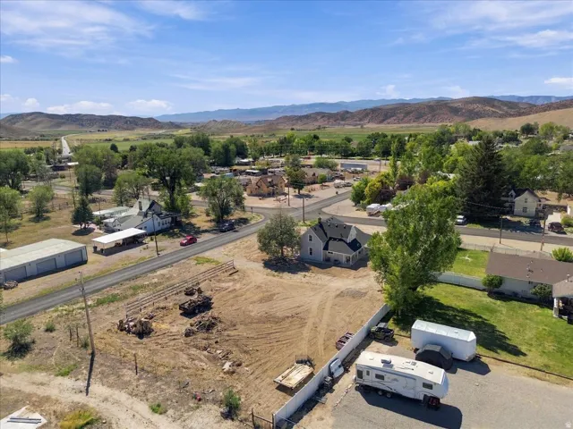 Expansive rural landscape with distant mountains, featuring a residential property with a light-colored exterior and a dark roof, surrounded by mature trees