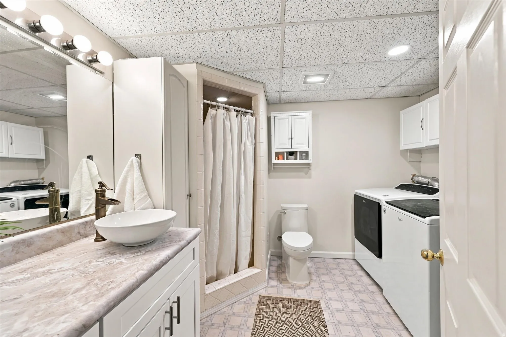 Full bathroom featuring a pedestal sink, shower, toilet, and laundry area