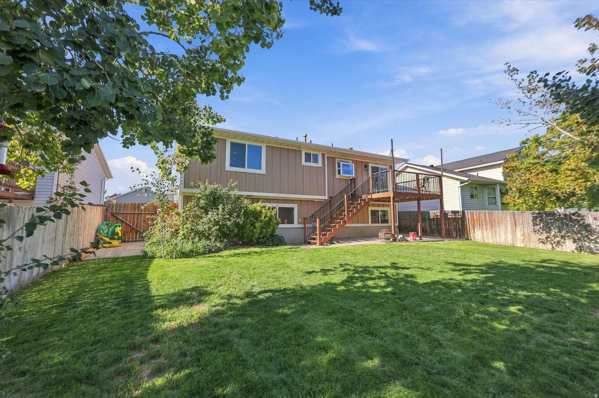 Expansive fenced backyard with a wood deck featuring stairs to the ground level, and a lower patio area