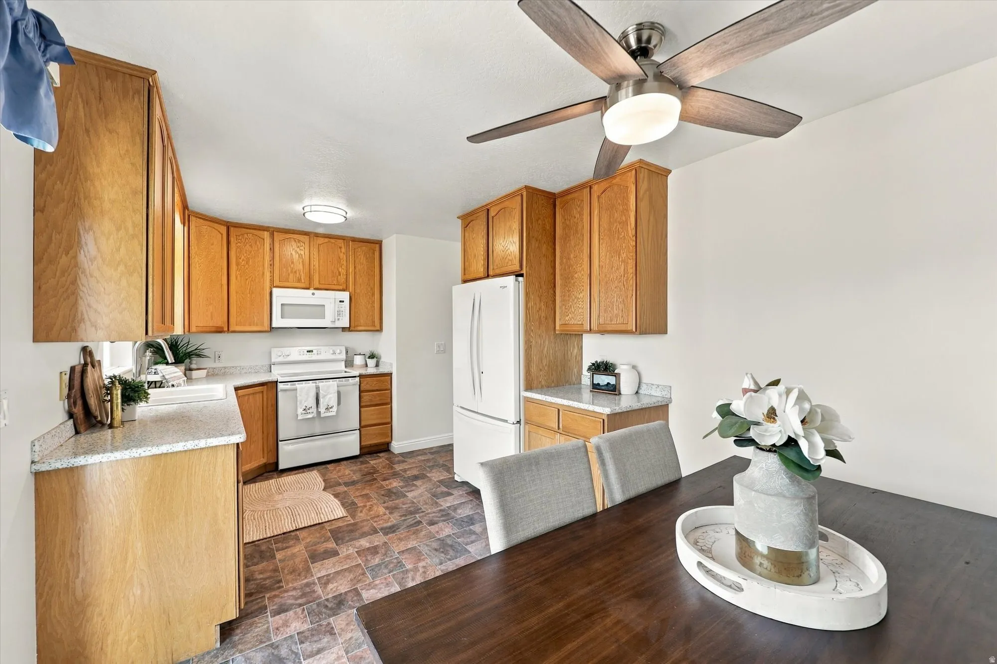 Kitchen featuring wood cabinetry, white appliances, a ceiling fan with light, and speckled countertops