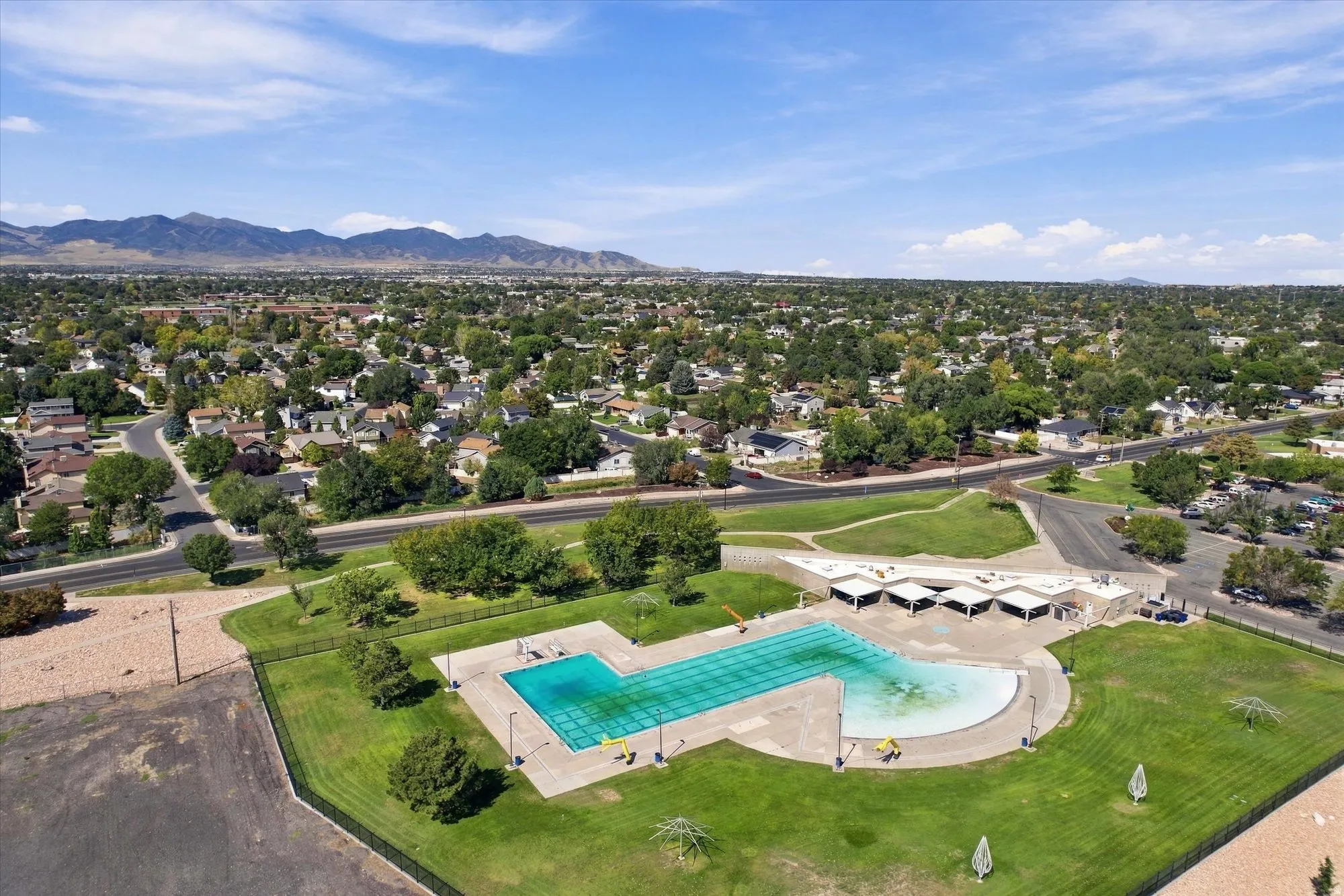 Community swimming pool with an adjacent wading area, surrounded by expansive green spaces and framed by distant mountains