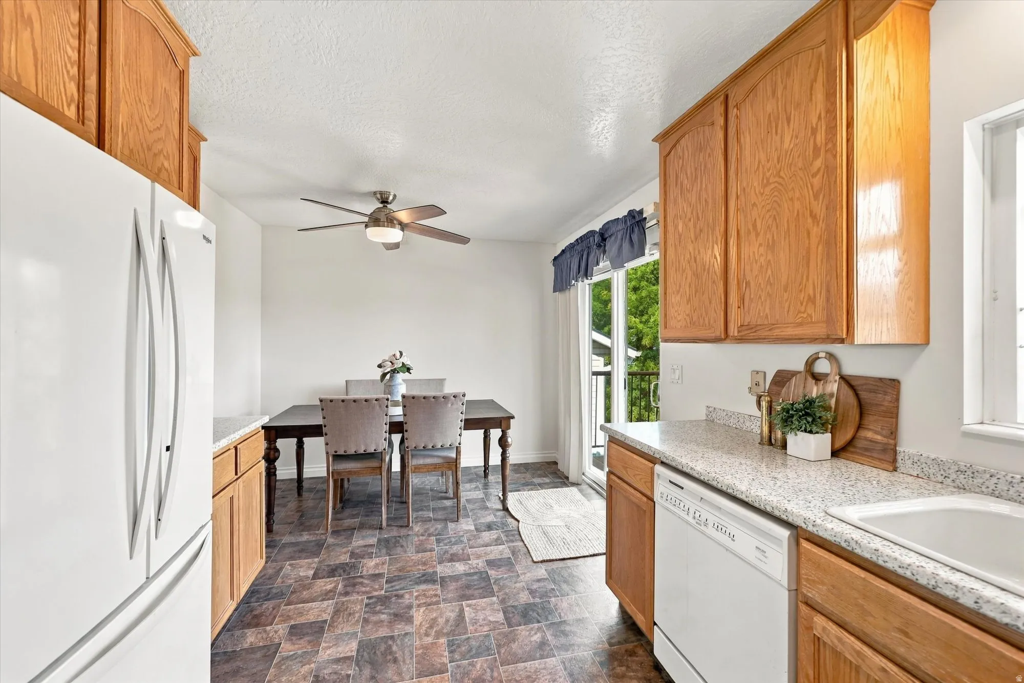 Light wood-finish cabinetry with white appliances, speckled countertops, and patterned floor tile