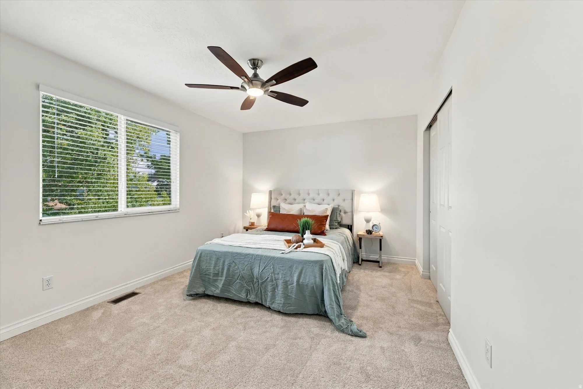 Carpeted flooring, white walls, window with blinds, and a ceiling fan with light fixture