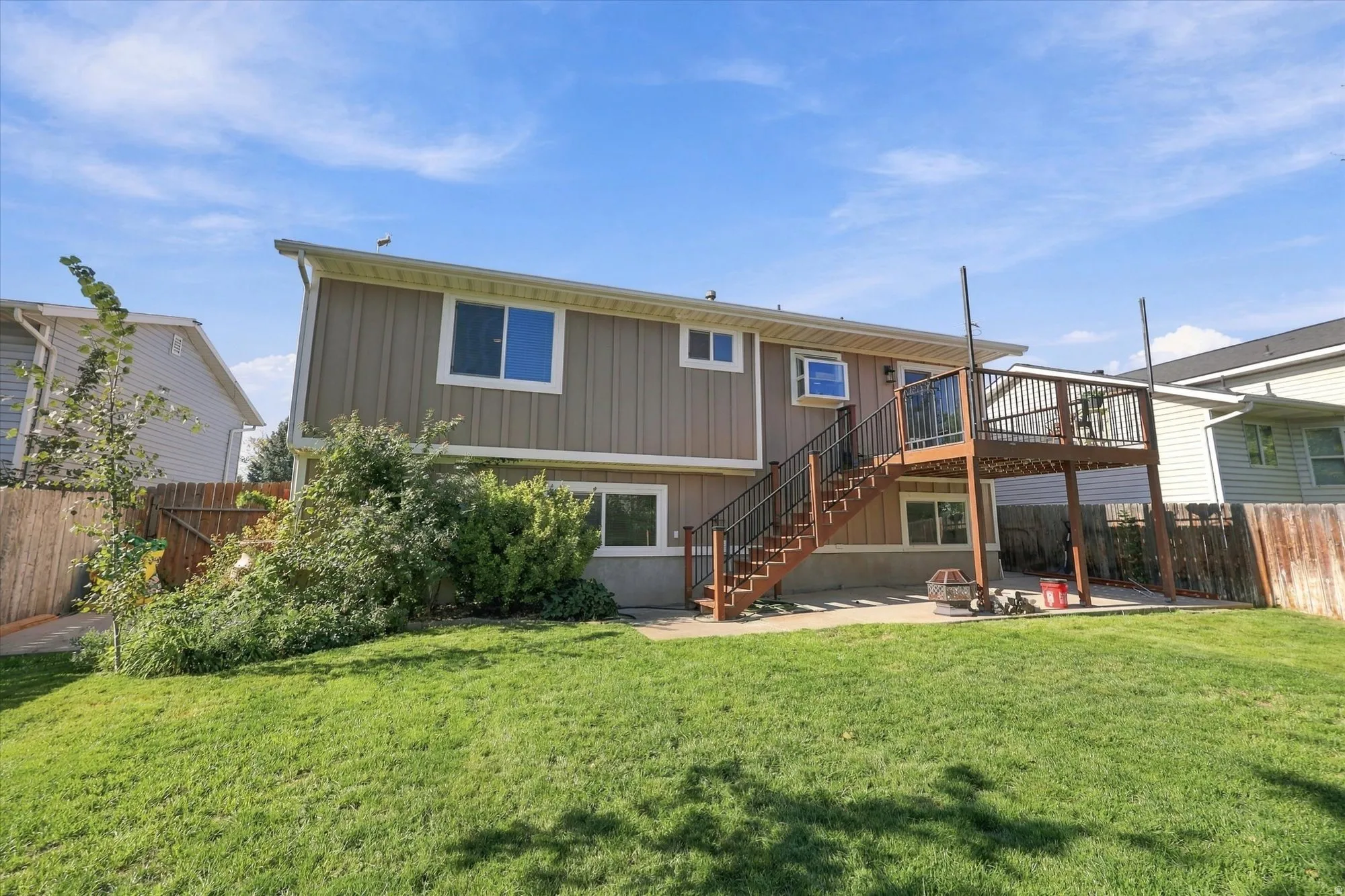Expansive backyard with a manicured lawn, multi-level exterior, and a wood deck featuring black metal railings