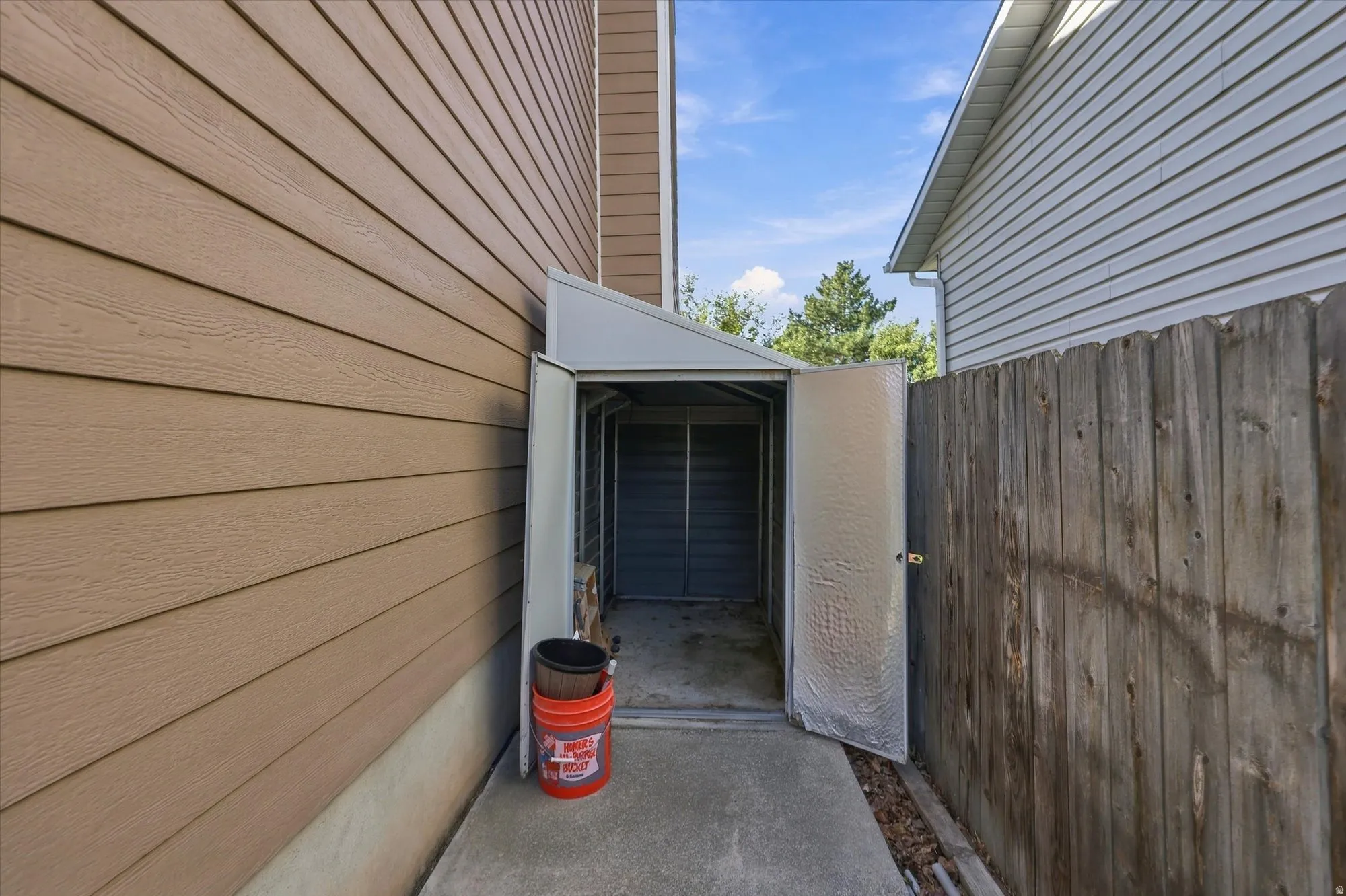 Exterior storage shed with metal door, wood-finish siding, and concrete walkway