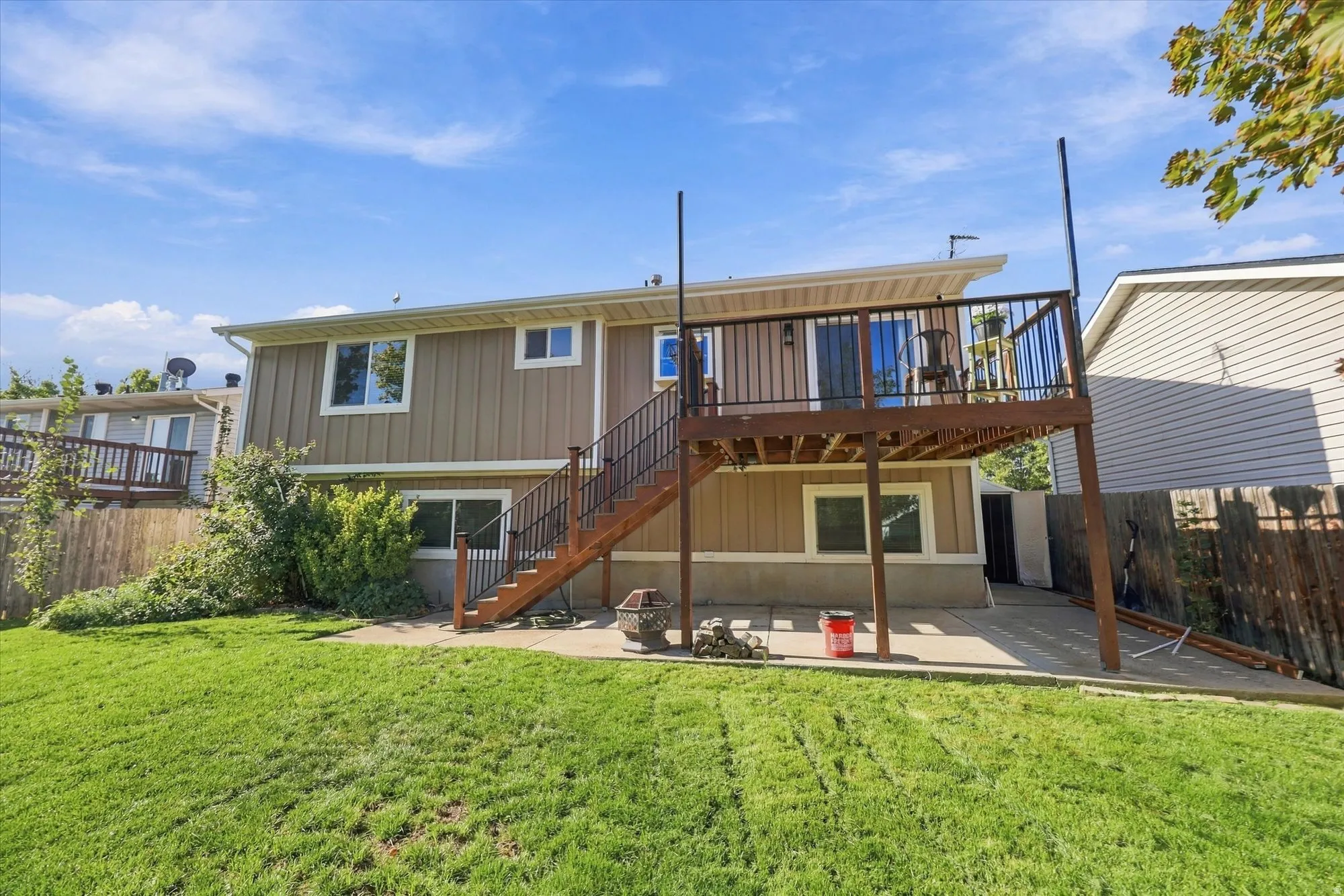 Expansive backyard featuring a manicured lawn, concrete patio, and a raised wood deck with metal railings