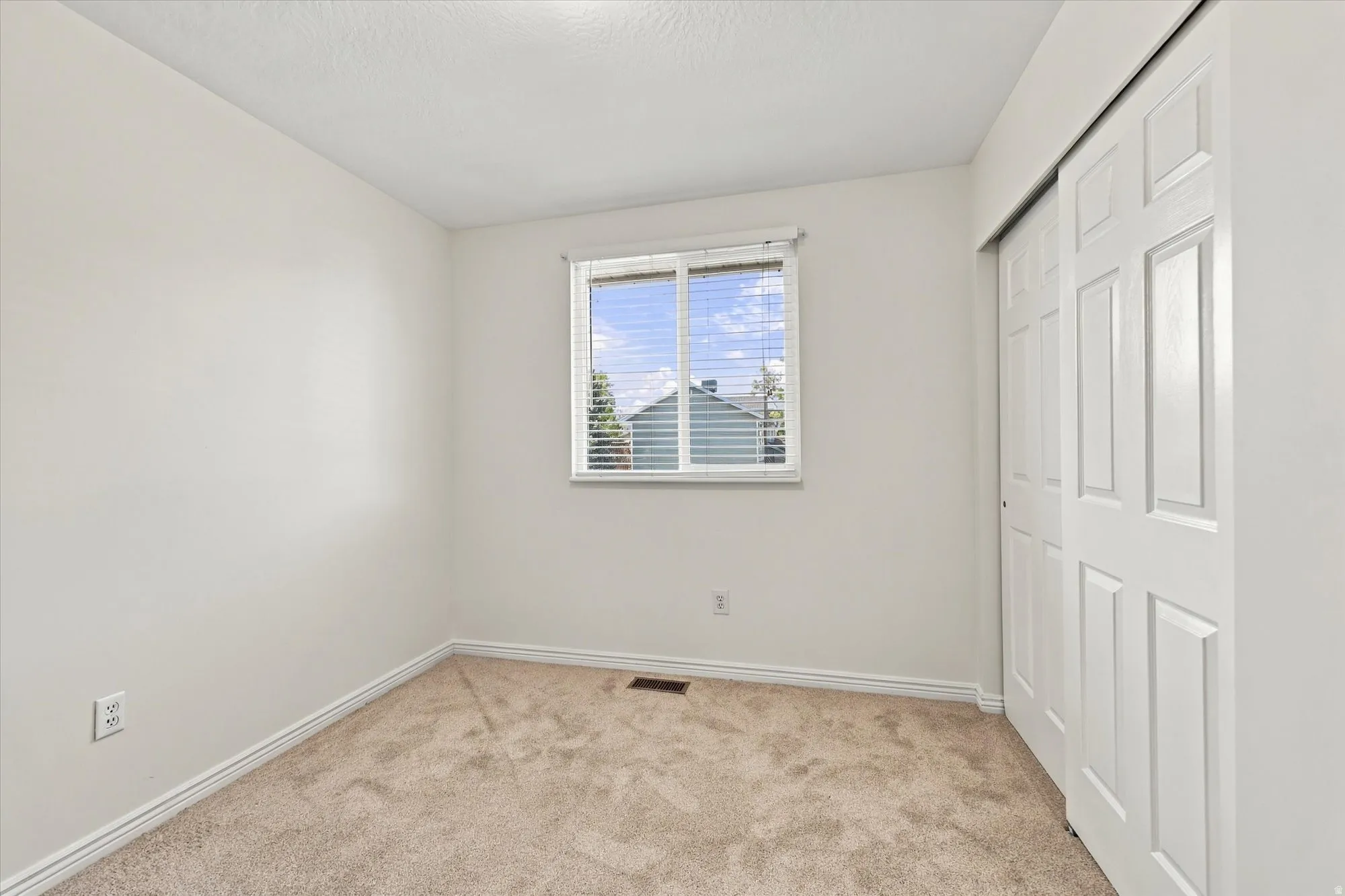 Neutral wall color, window with blinds, sliding closet doors, and carpeted flooring