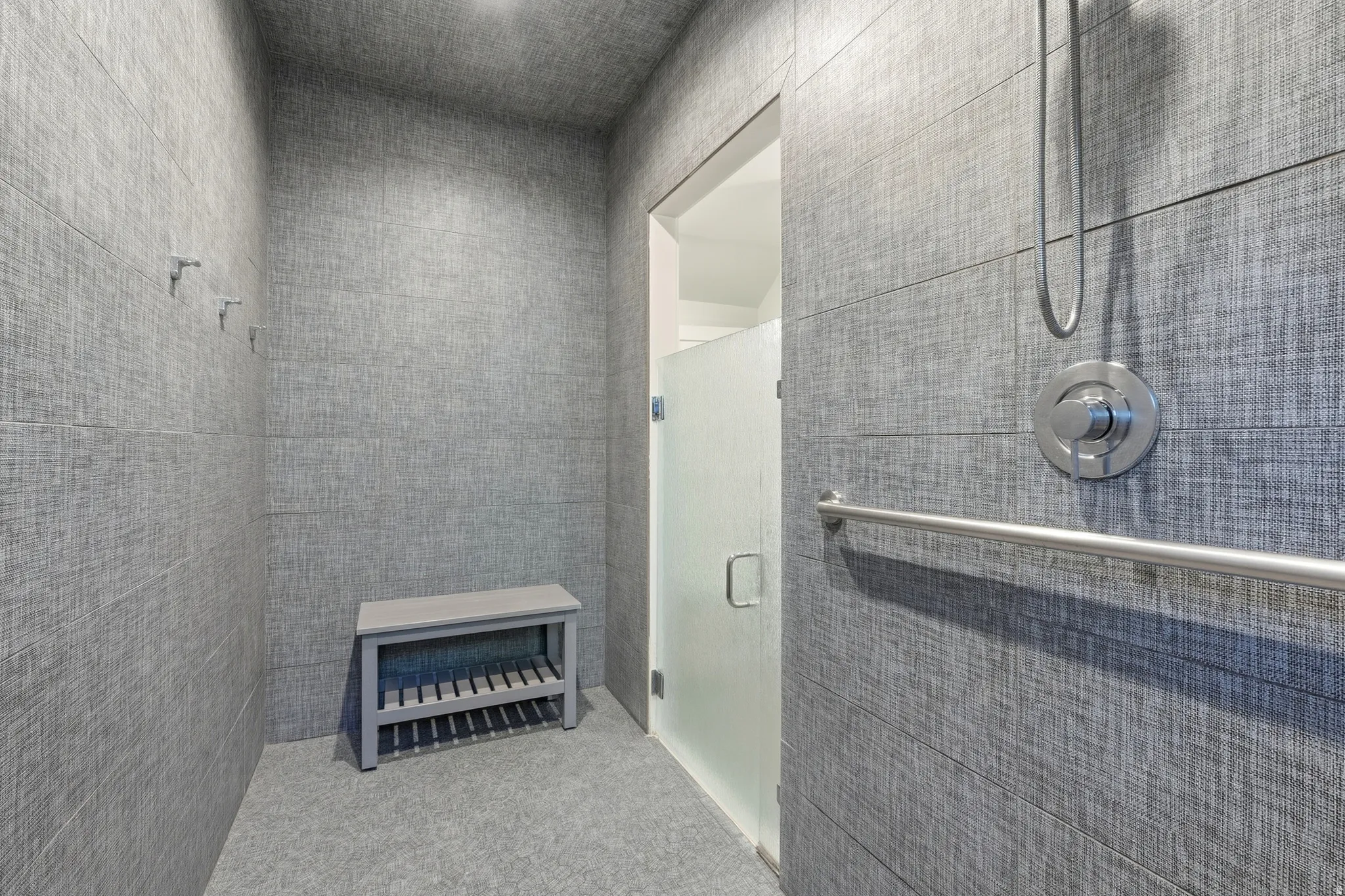 Textured gray wall tiling throughout, brushed nickel shower fixtures, and a frosted glass shower door