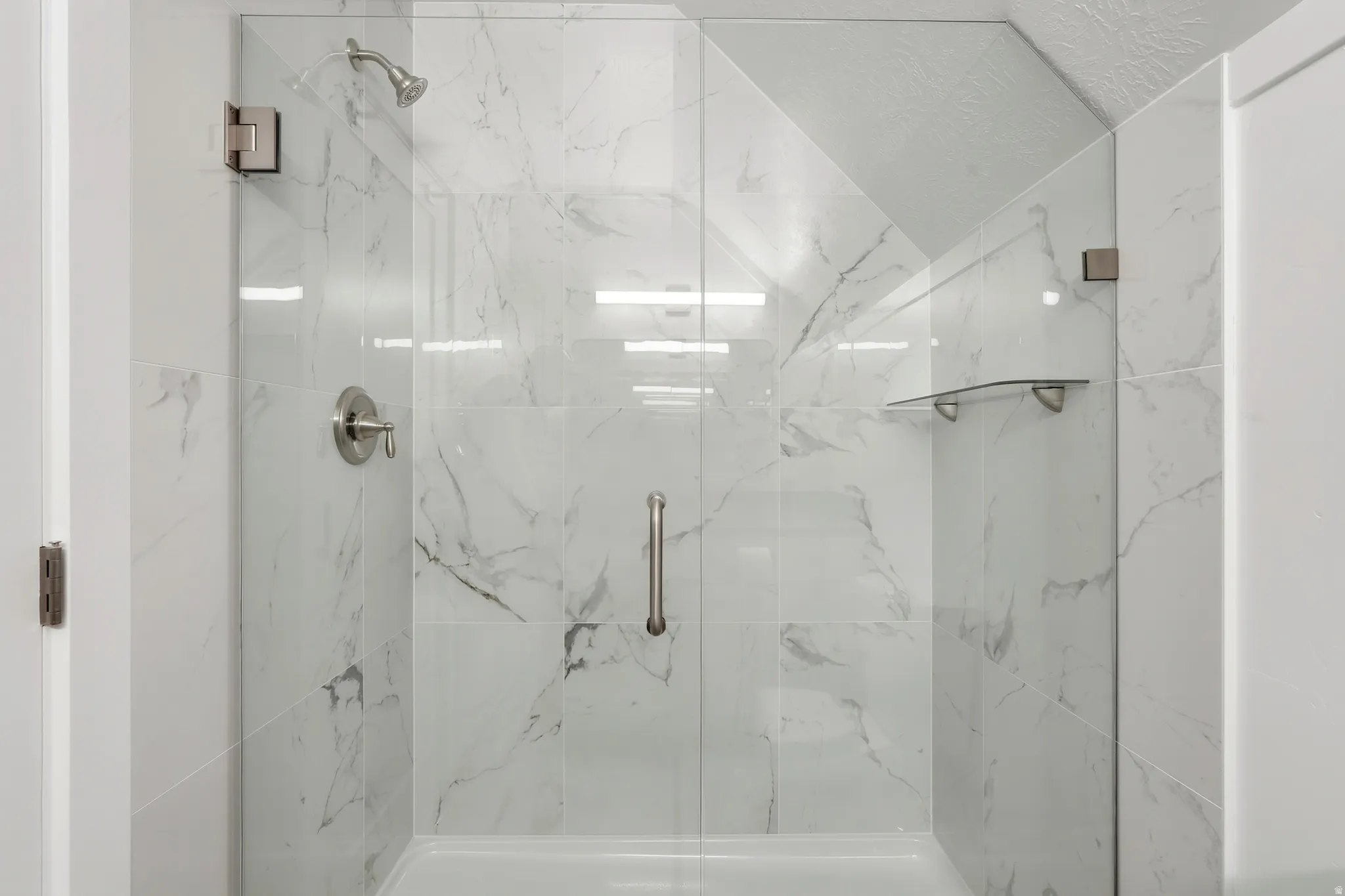 Glass-enclosed shower featuring large format tile, brushed nickel fixtures, a built-in shelf, and a textured ceiling