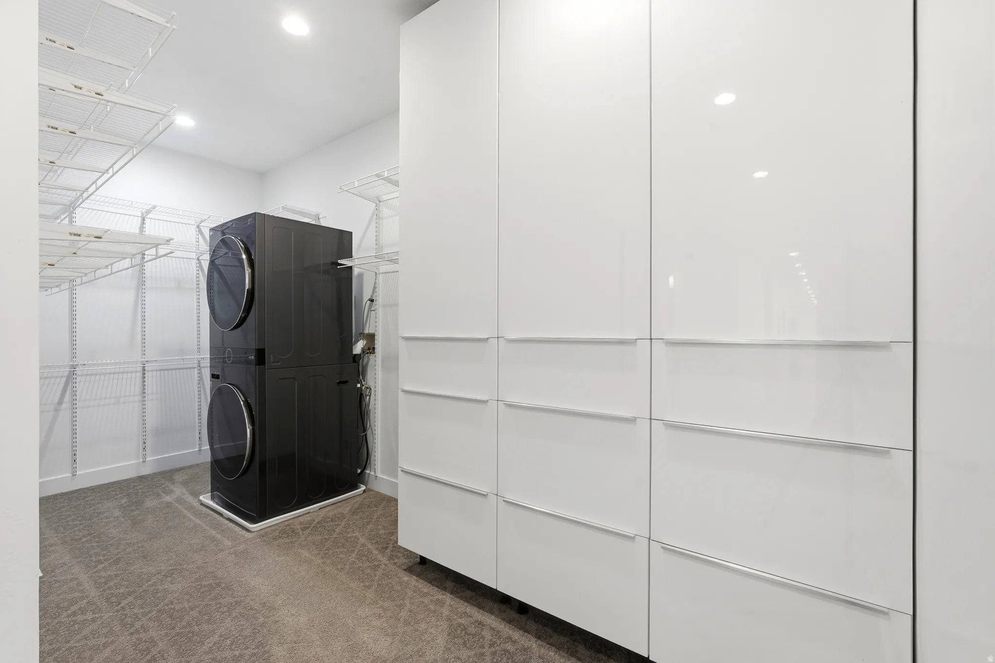 Laundry area featuring a stacked washer and dryer, wire shelving, and built-in white cabinetry with integrated hardware