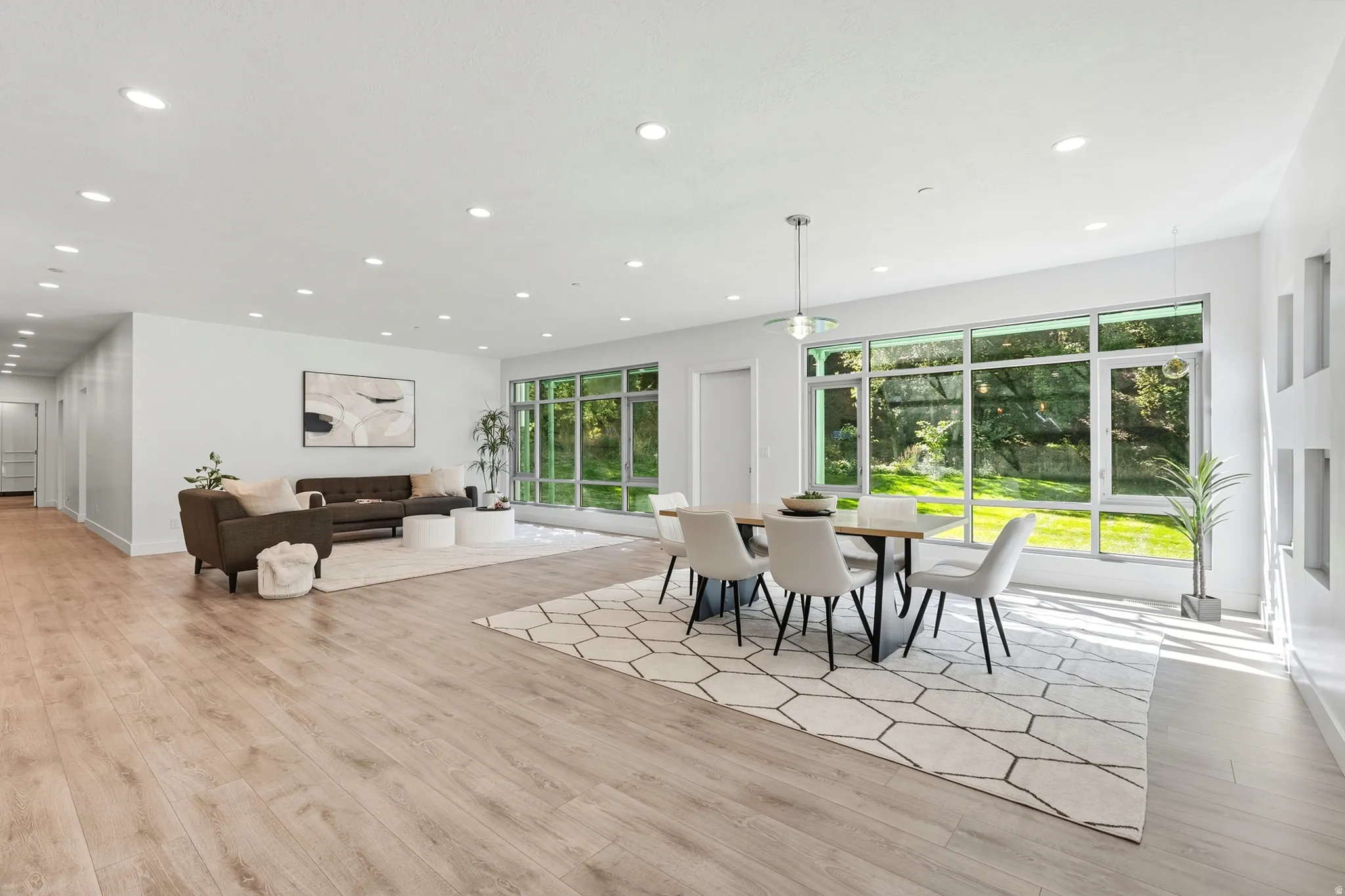 Open-concept living and dining area featuring wood-finish flooring, recessed lighting, and expansive windows