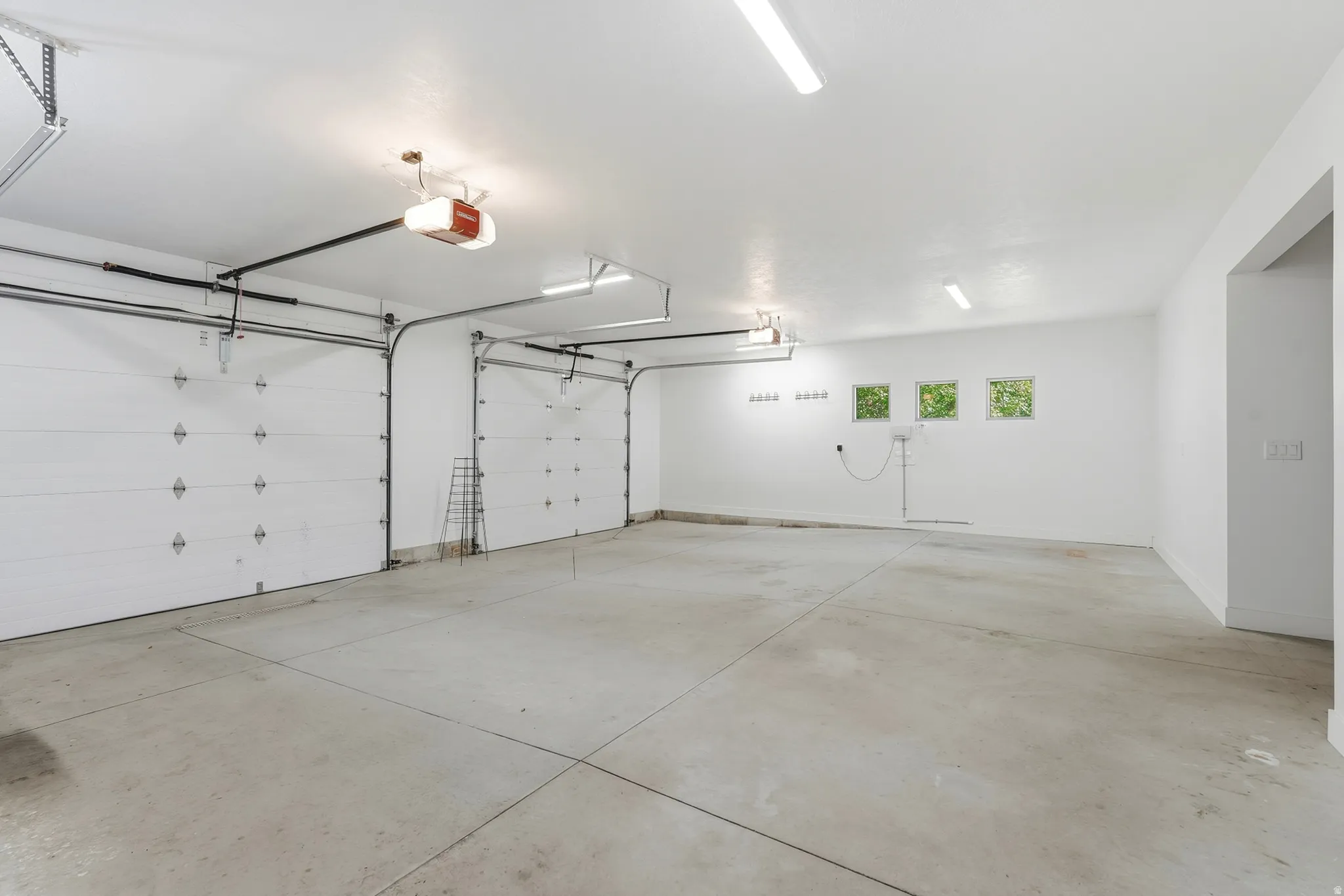 Two overhead garage doors with automatic openers, three transom windows, a concrete floor, and fluorescent ceiling lighting