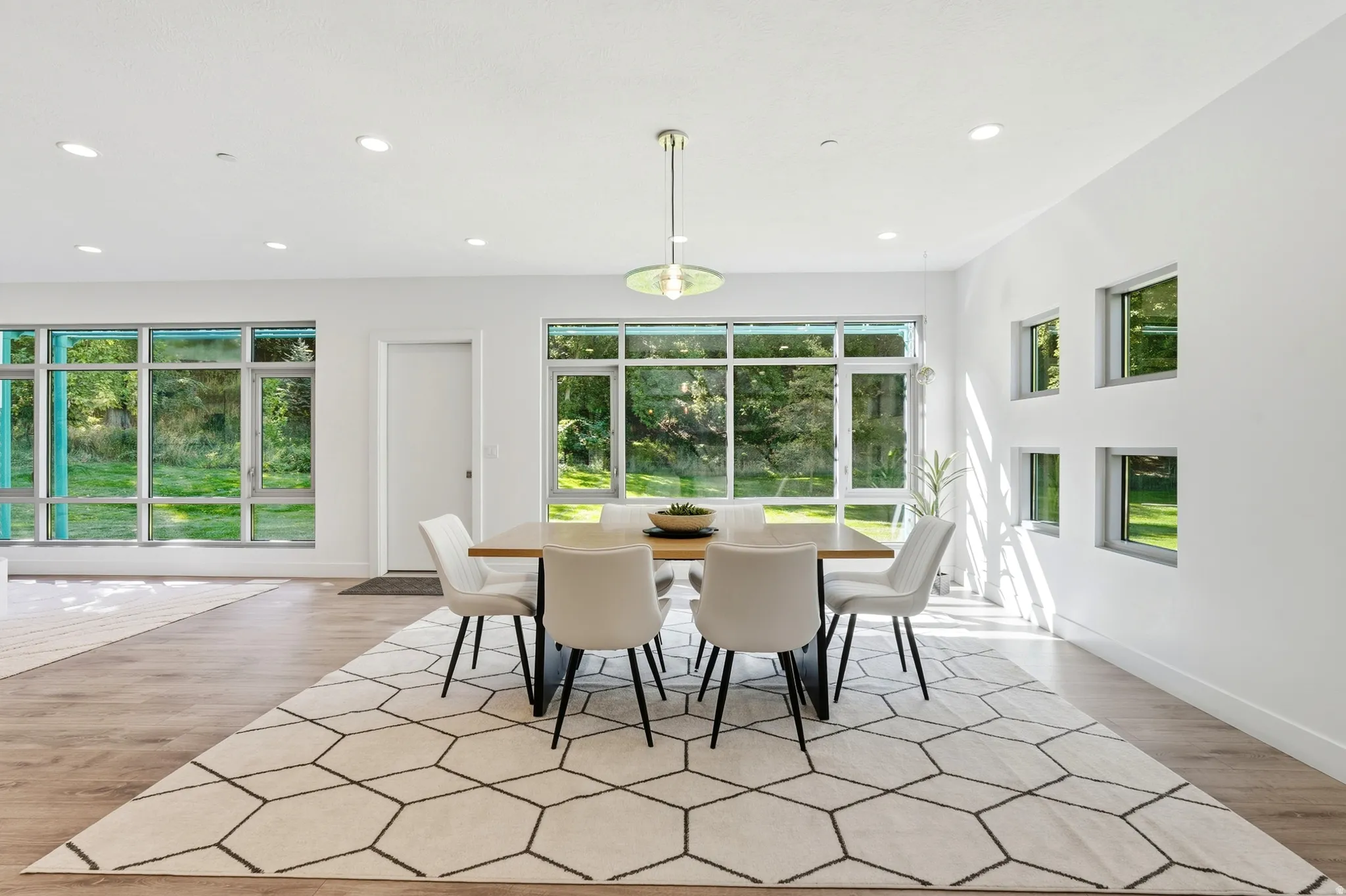 Recessed lighting throughout, wood-finish flooring, a modern pendant light fixture, and multiple large windows with exterior scenery