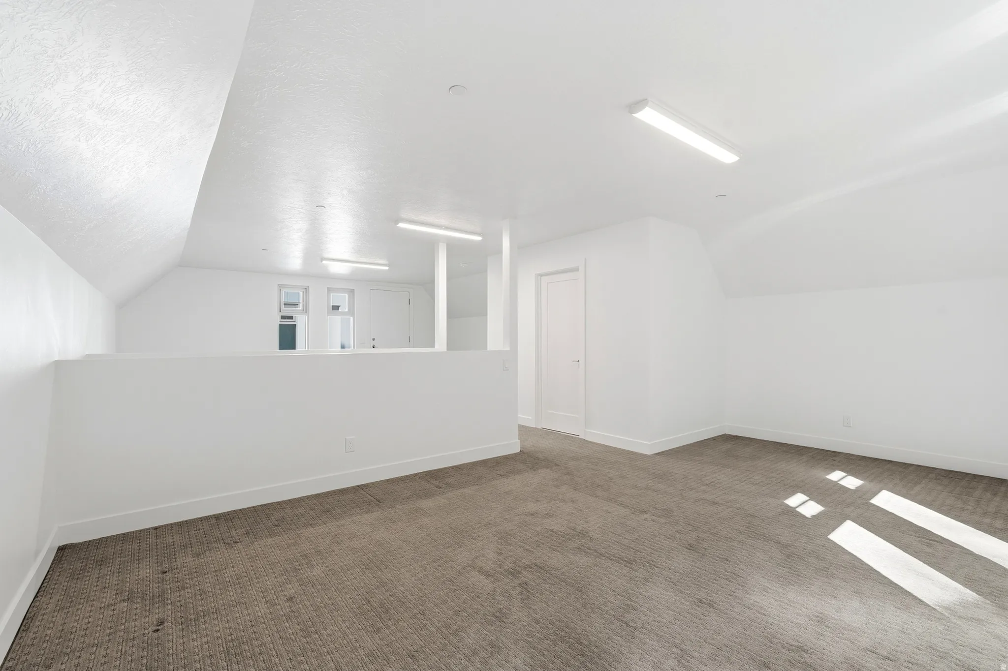 Carpeted loft space with sloped ceilings, recessed lighting, and a partial wall separation