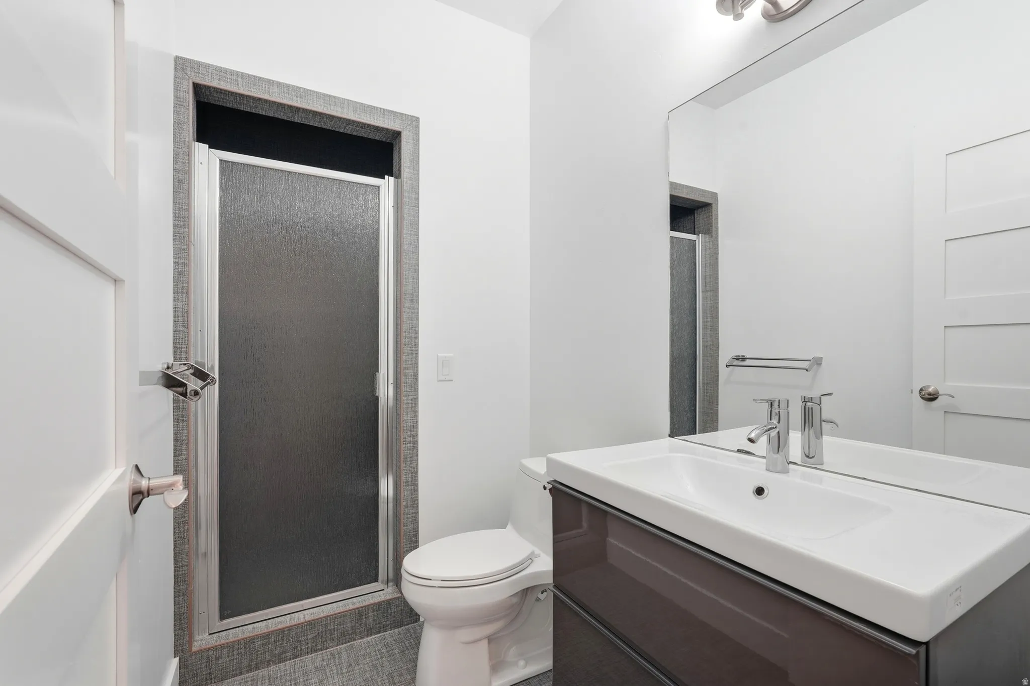 Vanity with integrated sink and chrome faucet, frameless mirror, and stall shower with textured glass door