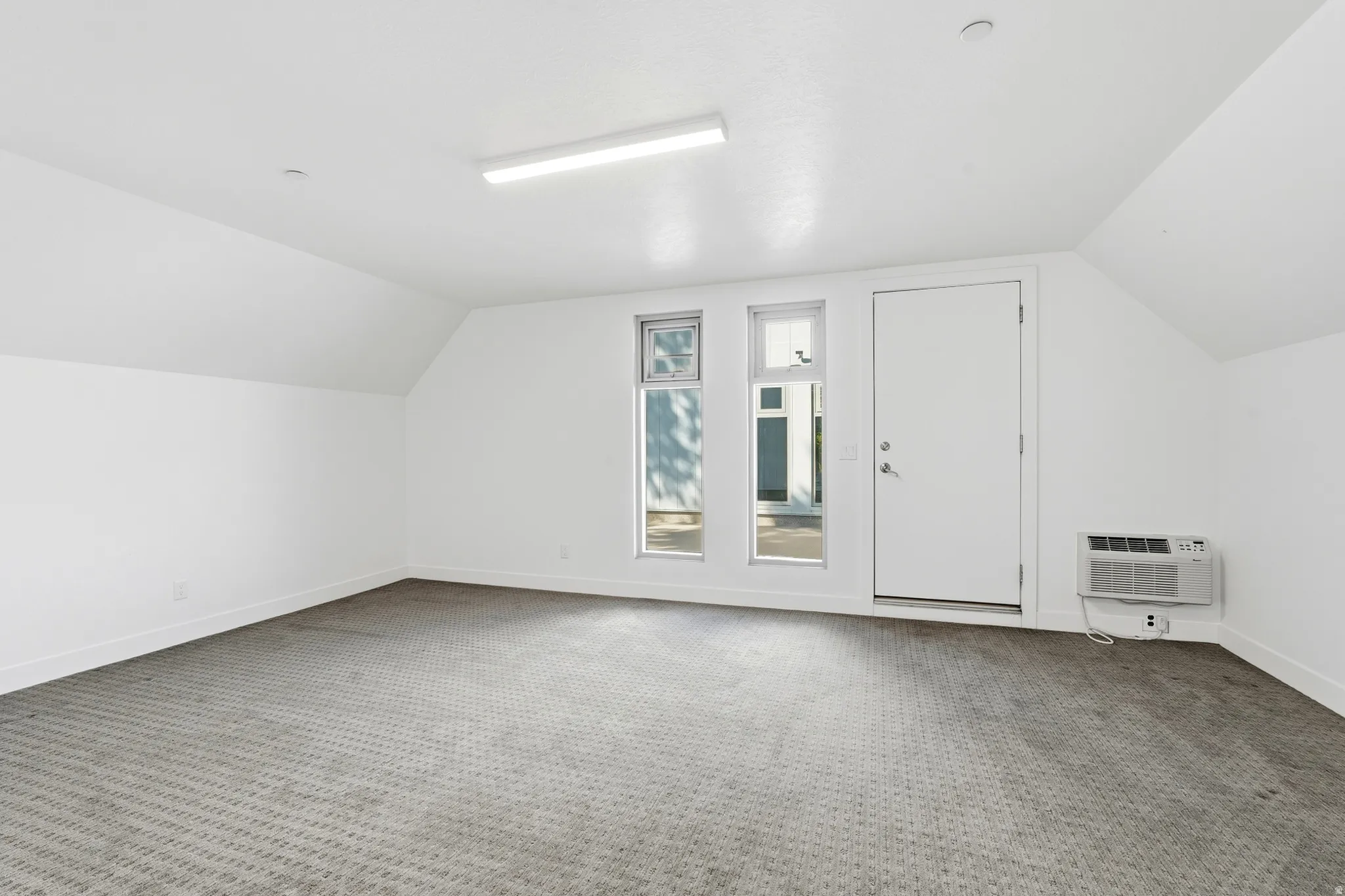 Spacious room featuring textured carpeting, white painted walls, and an angled ceiling