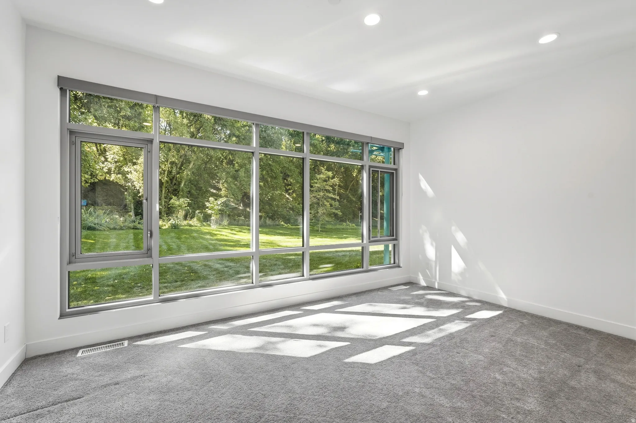 Expansive floor-to-ceiling windows with modern gray frames, recessed ceiling lighting, light gray carpeting, and crisp white walls